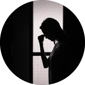 Silhouette of woman standing in front of window, holding the bridge of her nose.