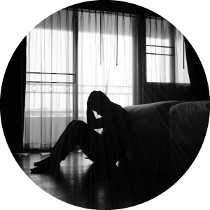 Silhouette of man sitting at the foot of his bed, head in his hands, looking depressed.