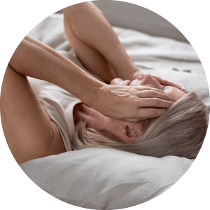 Woman laying on bed, head in her hands, looking like she is in pain.